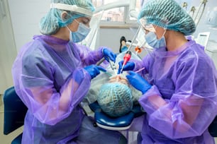 a competent dentist and his assistant perform the operation in the office to install a dental implant. Dentistry concept