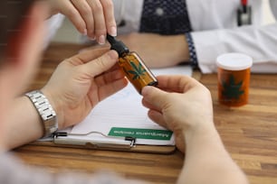 Nahaufnahme von Patientenhänden, die eine Flasche mit Cannabinoidöl halten. Ärztin bereitet Marihuana-Rezept zu. Volksheilkunde und alternatives Therapiekonzept