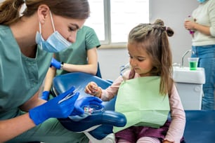 Giovane dentista specializzata qualificata che lava i denti di un bambino piccolo che è stato portato alla reception. Il concetto di lavarsi i denti da latte