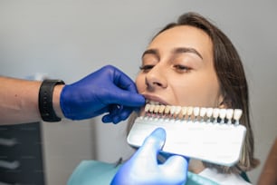Una mujer habla sobre el blanqueamiento dental con su dentista con una tabla de muestra junto a sus dientes. Concepto de blanqueamiento dental. Selección del tono de los dientes