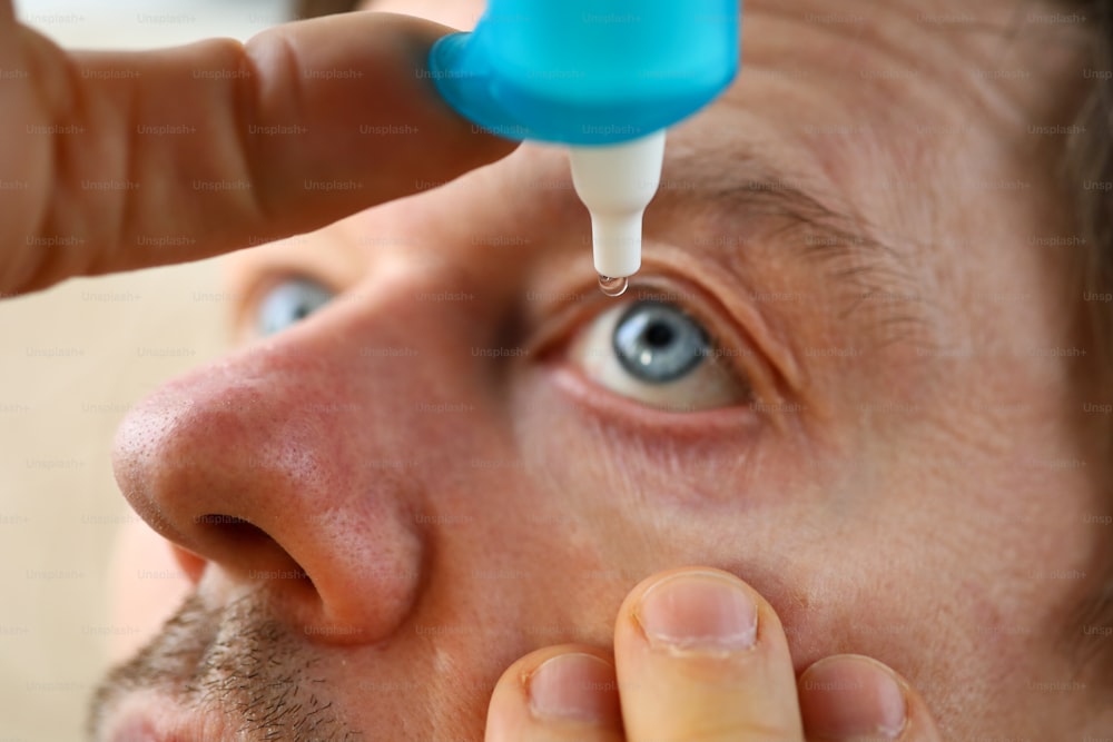 Mano masculina que pone gotas líquidas en su ojo resolviendo el problema de la visión de cerca
