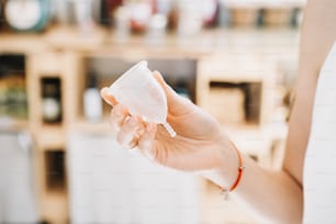 Girl holding in hands menstrual cup in sustainable plastic free store. Reusable female supplies for intimate hygiene. Woman buying modern alternative personal hygiene items in zero waste shop