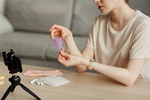 Minimal closeup of young woman holding menstrual cup and filming educational video on feminine hygiene products