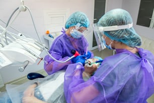 Un paciente con un problema de dientes encarnados yace en un sillón de operaciones donde es operado por un dentista y sus asistentes. El concepto de cirugía en el dentista