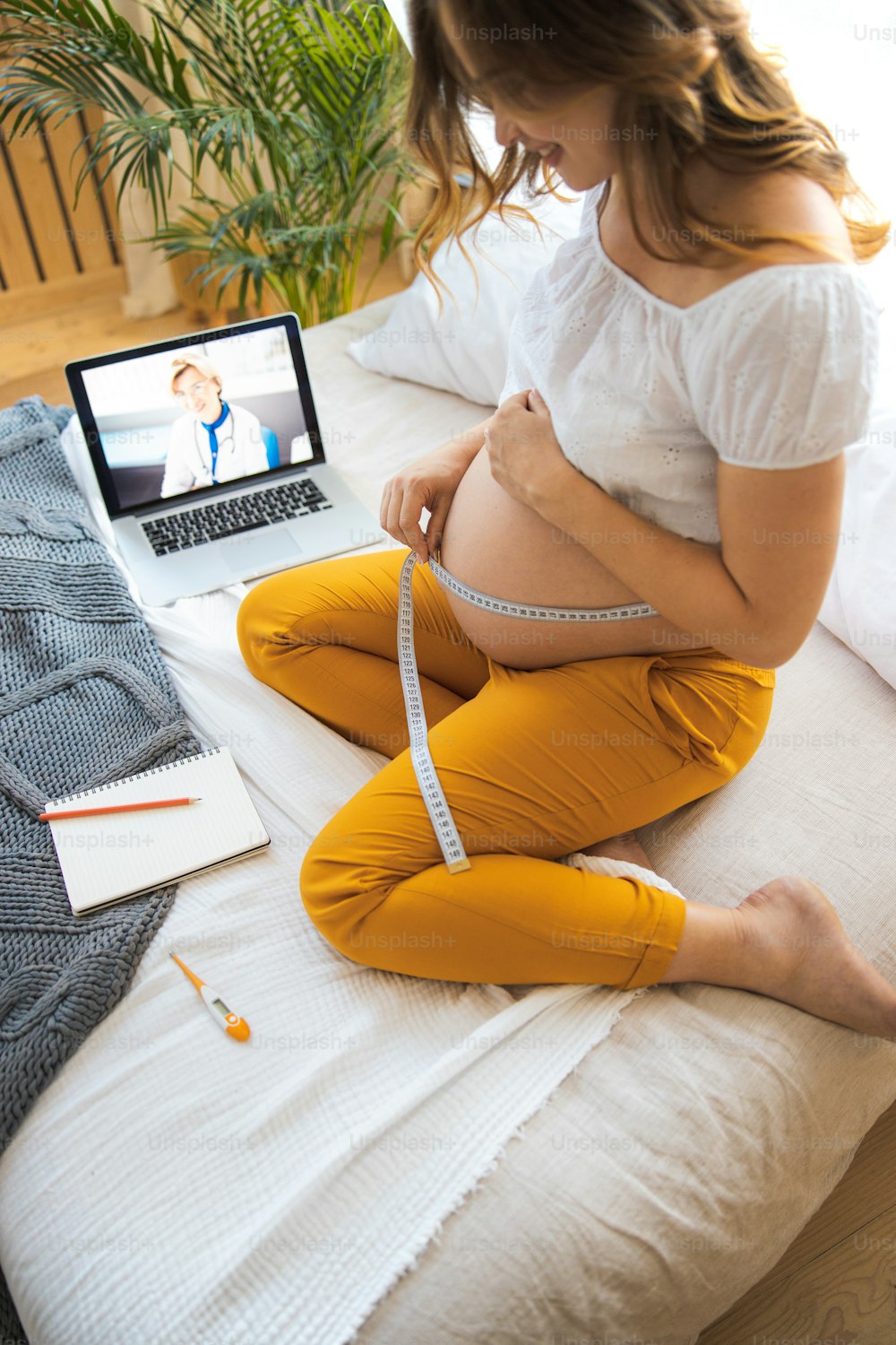 Smiling expectant mother talking with doctor through video call and checking growth of her belly stock photo