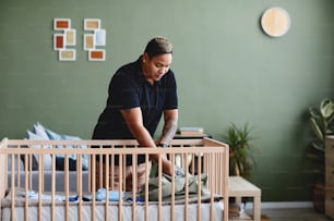 Portrait of tattooed gay woman preparing baby crib in minimal home interior, copy space
