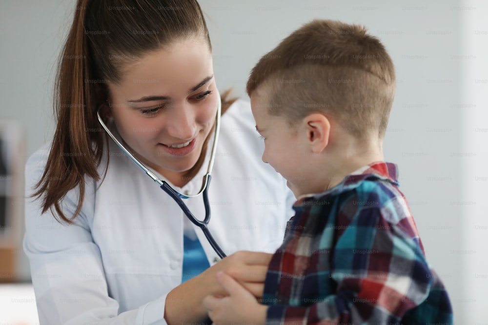 Porträt einer jungen Kinderärztin, die Kind mit Stethoskop-Werkzeug bei geplanter Untersuchung abhört. Termin in der Klinik zur Untersuchung des Gesundheitszustands. Gesundheitskonzept