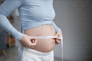 Minimal closeup of pregnant young woman measuring belly with tape, copy space