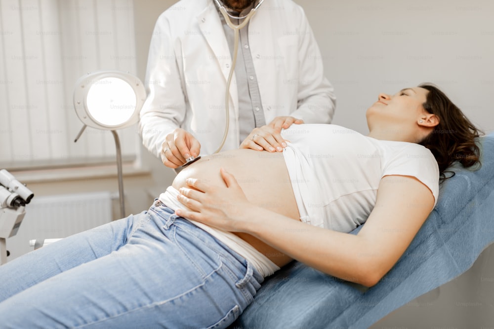 Doctor listening to a pregnant woman's belly with a stethoscope during a medical examination. Concept of medical care and health during a pregnancy