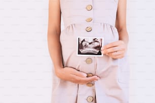 Pregnant woman holding ultrasound baby image. Close-up of pregnant belly and sonogram photo in hands of mother. Concept of pregnancy, gynecology, medical test, maternal health.