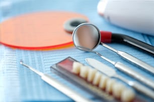 Dentures and metal dental instruments lying on blue sterile napkin closeup. Dental health care concept