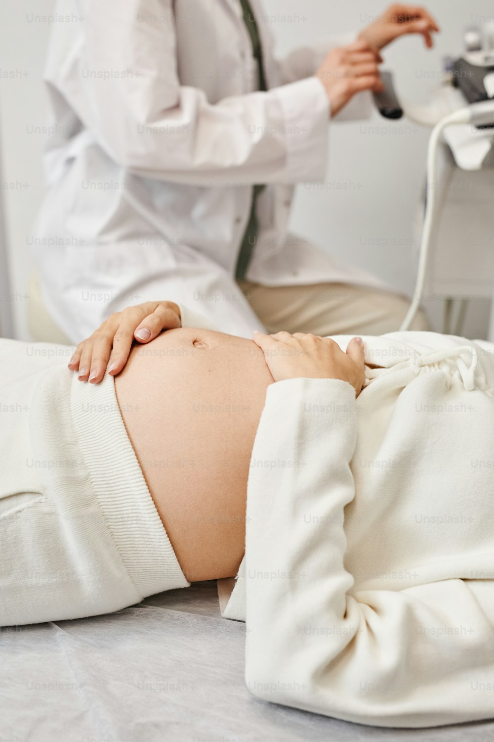 Vertical closeup of pregnant young woman preparing for ultrasound in medical clinic with focus on belly