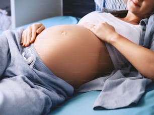 Primer plano del hermoso vientre embarazada de la mujer acostada en la cama. Futura madre abrazando su vientre y descansando. Madre amorosa esperando a un bebé. Concepto de embarazo, maternidad, salud, ginecología.