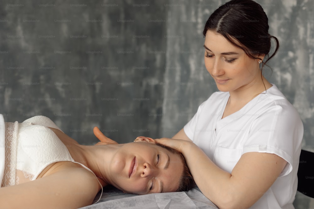 Osteopath in medical cabinet massage cervical vertebrae of woman lying down on hospital couch in white underwear. Professional specialist appointment and examination, healthcare and disease treatment.