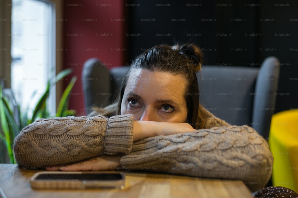 Pensive millennial woman having bad day lying with head on hand on table near window at cafe, lost in unpleasant thoughts. Melancholy, disappointment, indifference