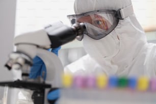 Ein Mann in Schutzanzug und Maske schaut durch ein Mikroskop, Nahaufnahme. Forschungslabor für gefährliche Viren
