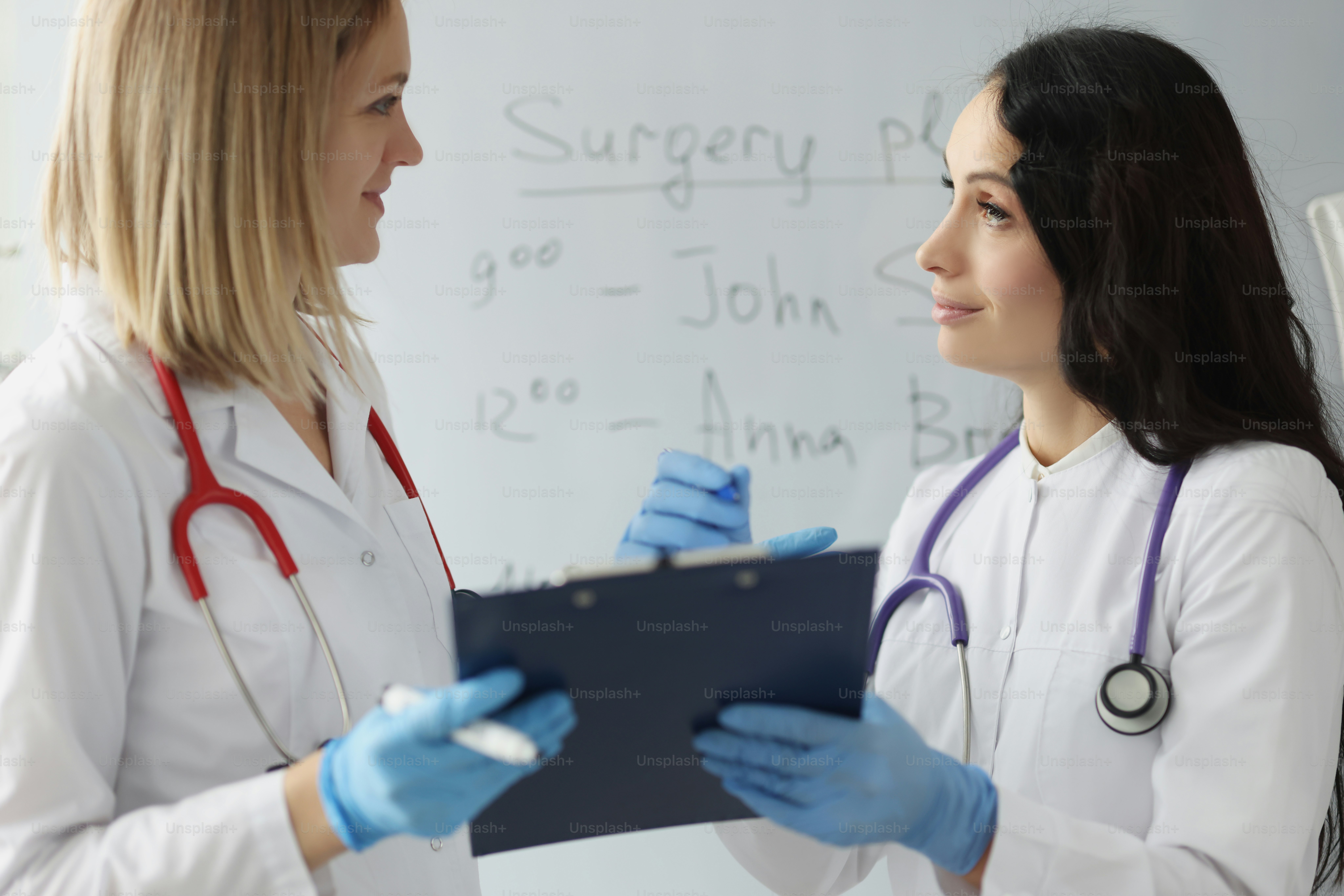 Female surgeons holding clipboard with documents and discussing schedule of operations in clinic. Surgical planning concept