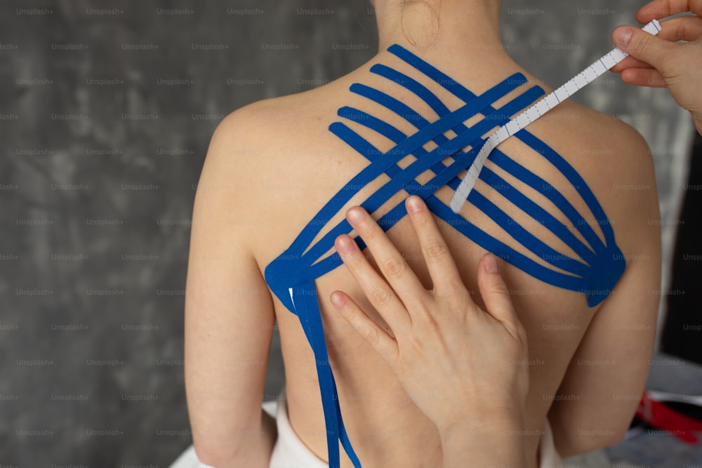 Unrecognizable cropped doctor, physiotherapist hand apply kinesio tapes on back muscles. Kinesiology therapy treatment. Female patient feel pain, backache after sport training. Athlete traumatic rehab