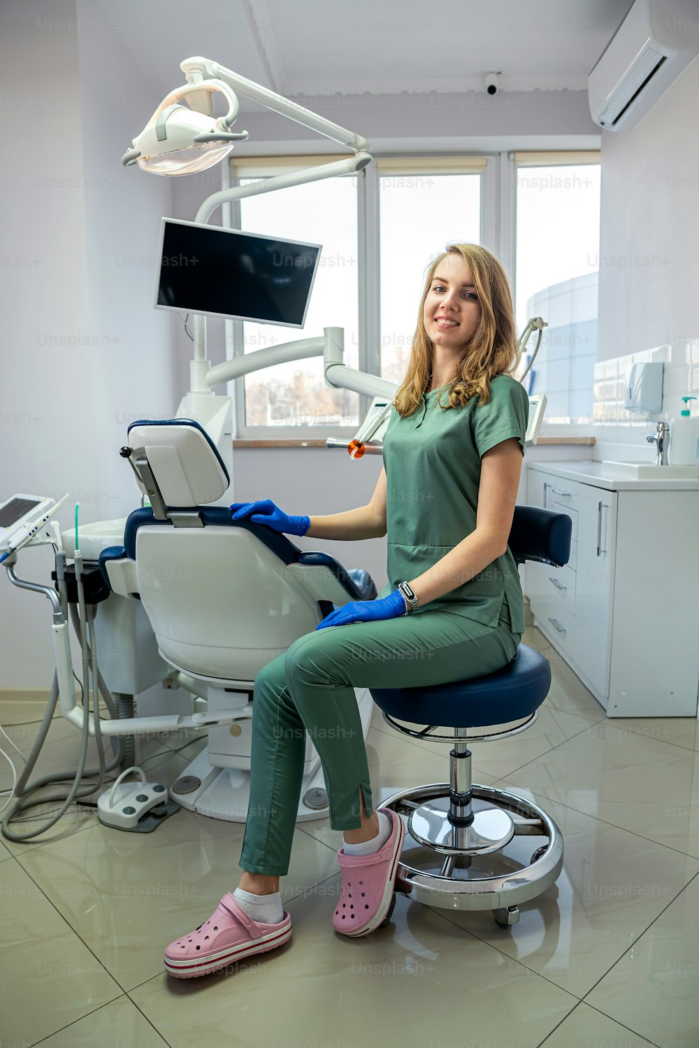 Young woman dentist in uniform and protection gloves posign alone at clinic. health care