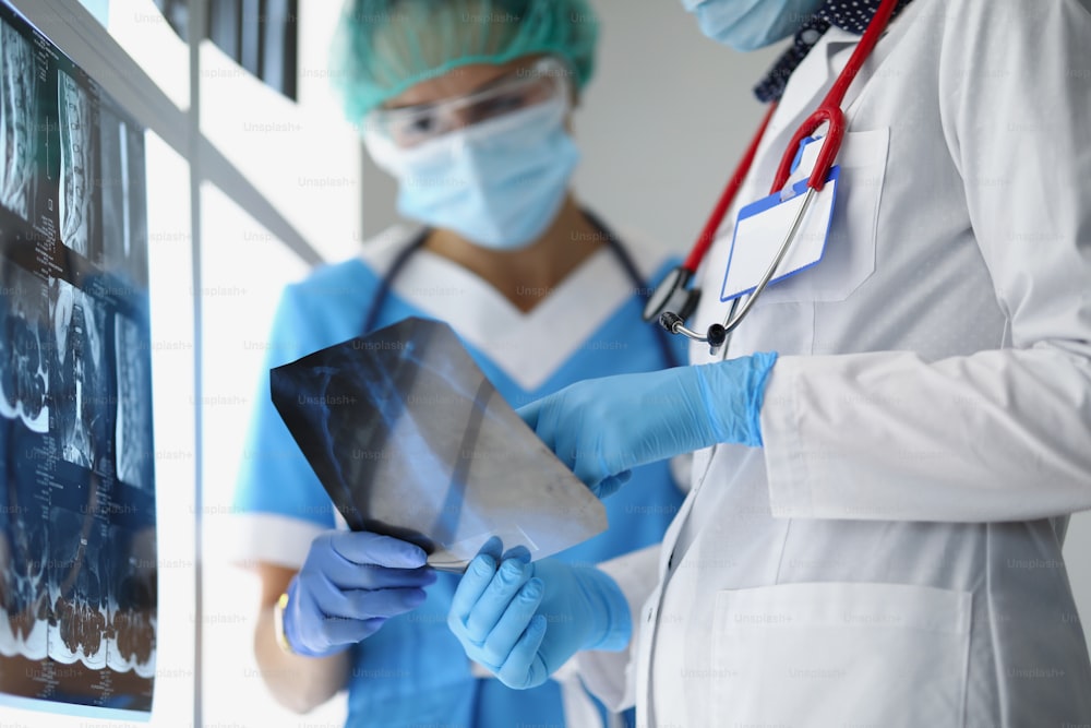 Close-up of nurse and professional medical doctor holding x ray screen with patients results. White lab coat and blue gloves. Stethoscope device on neck. Medicine and healthcare concept