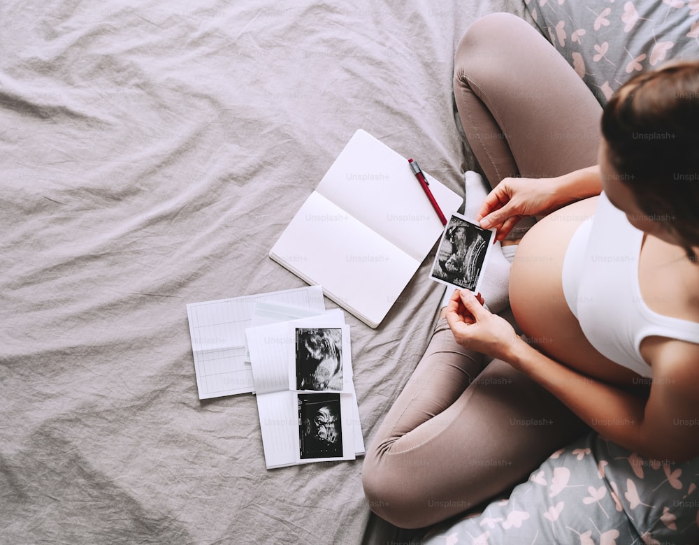 Pregnant woman holding ultrasound image looking at notebook and medical test reports. Expectant mother with pregnant belly waiting for baby. Concept of pregnancy, gynecologic, healthcare.