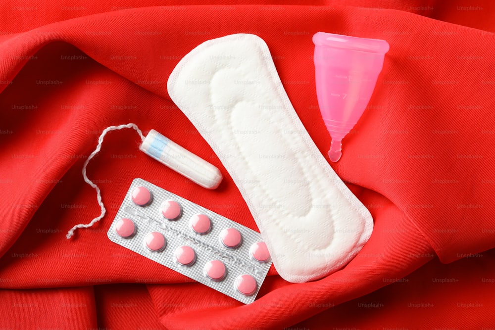 Toalla sanitaria, tampón, píldoras y copa menstrual sobre fondo rojo, vista superior