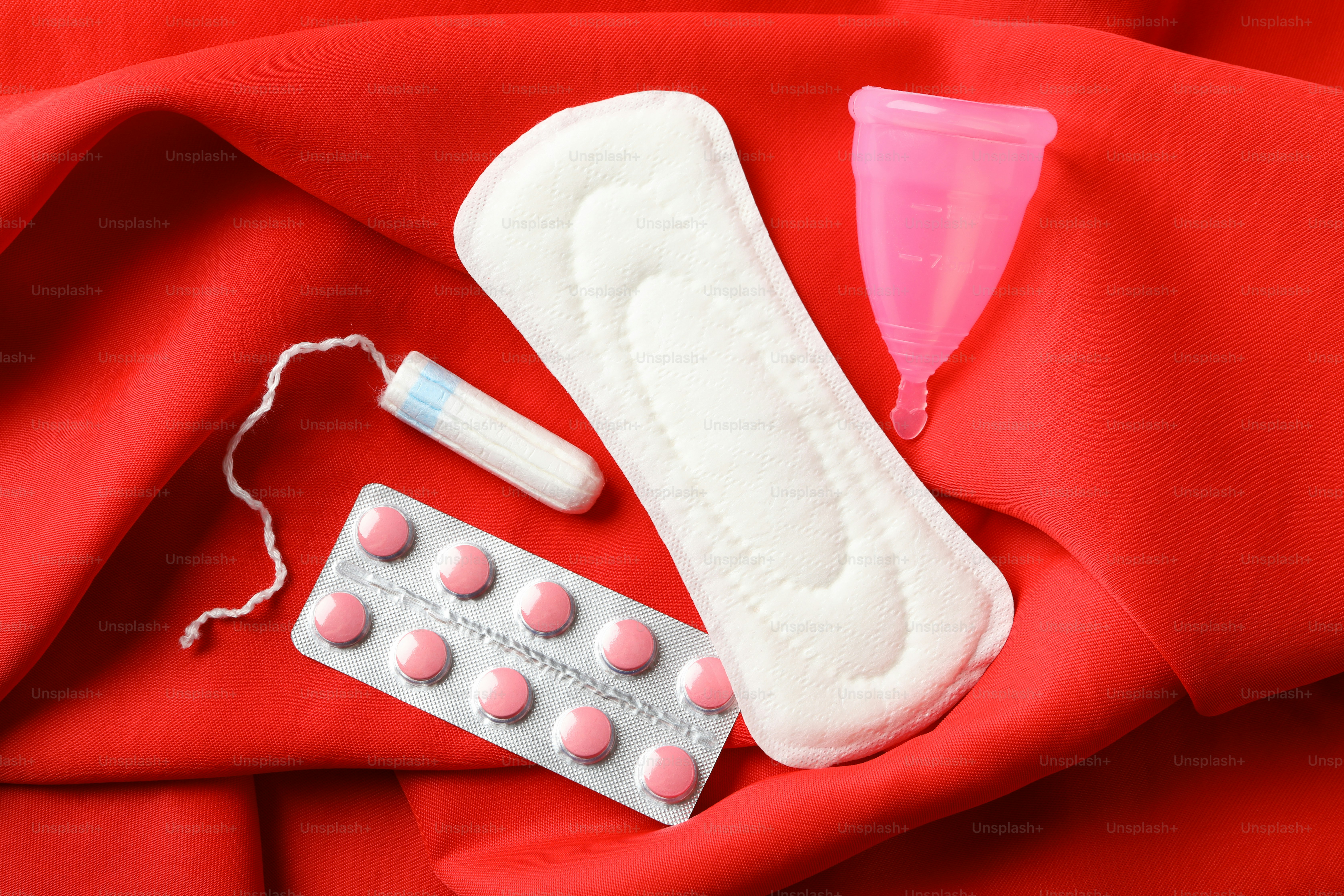 Sanitary pad, tampon, pills and menstrual cup on red background, top view