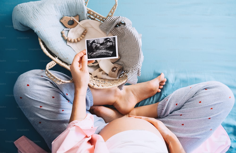 Pregnant woman looking at ultrasound images. Expectant mother waiting and preparing for baby birth during pregnancy. Mother with wicker basket of stuff for newborn child.