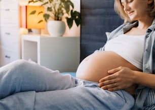 침대에 누워 있는 여자의 아름 다운 임신 배의 클로즈업. 배를 껴안고 쉬고 있는 임산부. 아기를 기다리는 사랑하는 어머니. 임신, 출산, 건강 관리, 부인과의 개념.