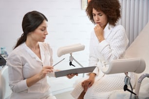 Une jeune femme est assise sur une chaise dans le bureau de la clinique et discute avec un gynécologue