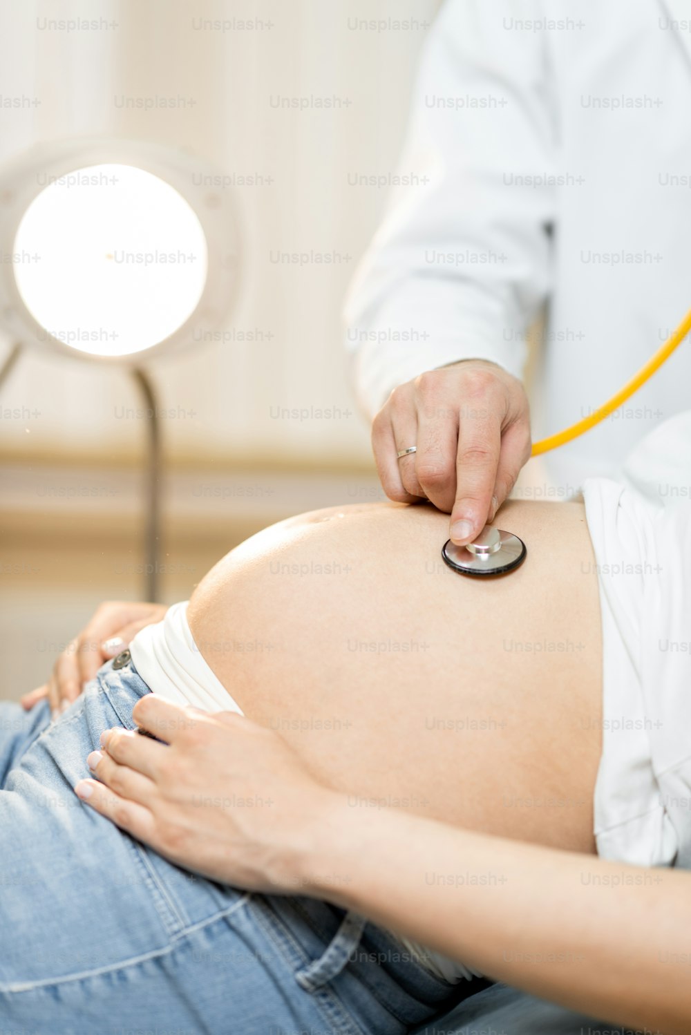 Doctor listening to a pregnant woman's belly with a stethoscope during a medical examination, close-up view