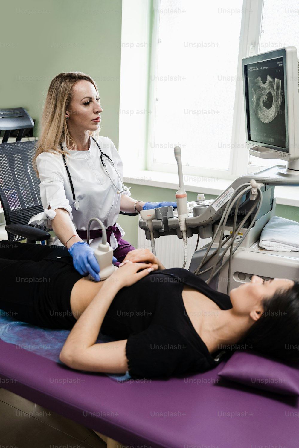 Pregnancy and maternity. Gynecologist conducts ultrasound scan for pregnant young woman on early pregnancy period and look on the screen in hospital