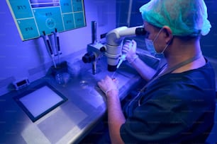 Laborant in sterile gloves and protective face mask looking at microscope, selecting healthy eggs and preparing them for fertilization in vitro