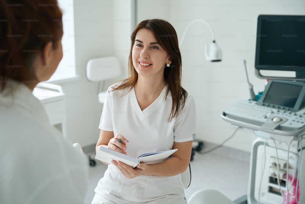 Terapeuta femminile allegra che ascolta il paziente e prende appunti dopo il controllo in clinica