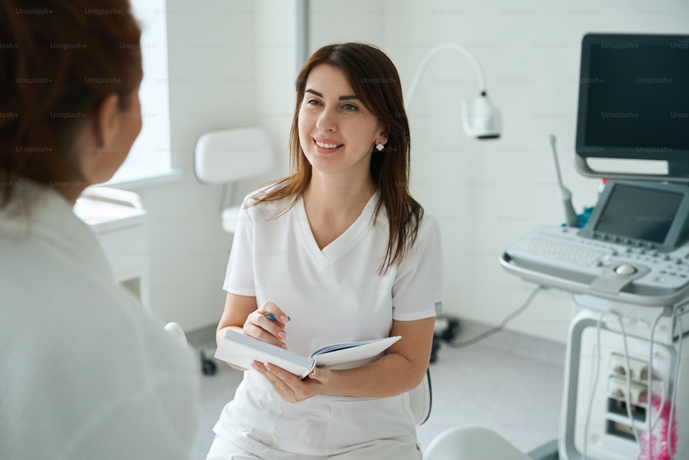 Femme thérapeute joyeuse à l’écoute du patient et prenant des notes après l’examen à la clinique