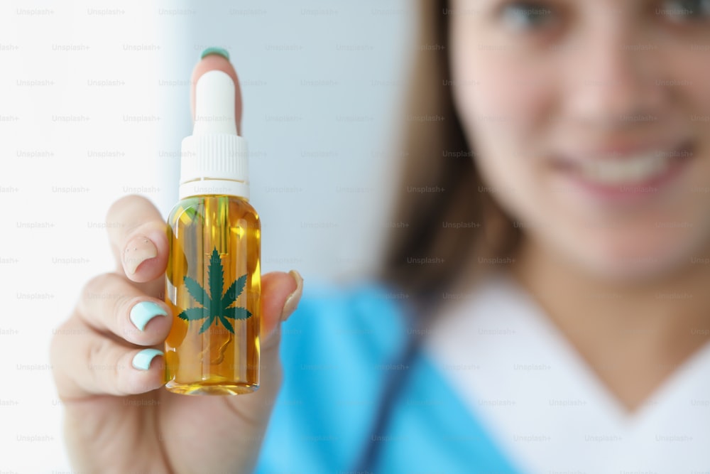 Close-up of medical worker present cannabis oil in plastic bottle for alternative treatment. Cute nurse prescribe hemp to patient. Medicine, health concept
