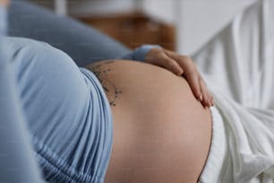 Side view of young woman with tattooed pregnant belly wearing blue, minimal