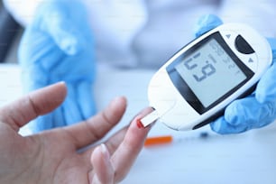Doctor measuring patients blood glucose with glucometer closeup. Diagnosis of diabetes concept