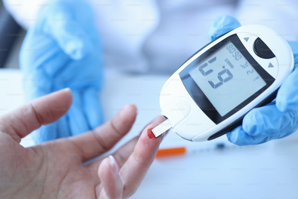 Doctor measuring patients blood glucose with glucometer closeup. Diagnosis of diabetes concept