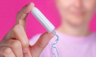 Mujer joven sosteniendo el tampón de la menstruación en la mano: cólicos menstruales de las mujeres. La menstruación, medios de protección.