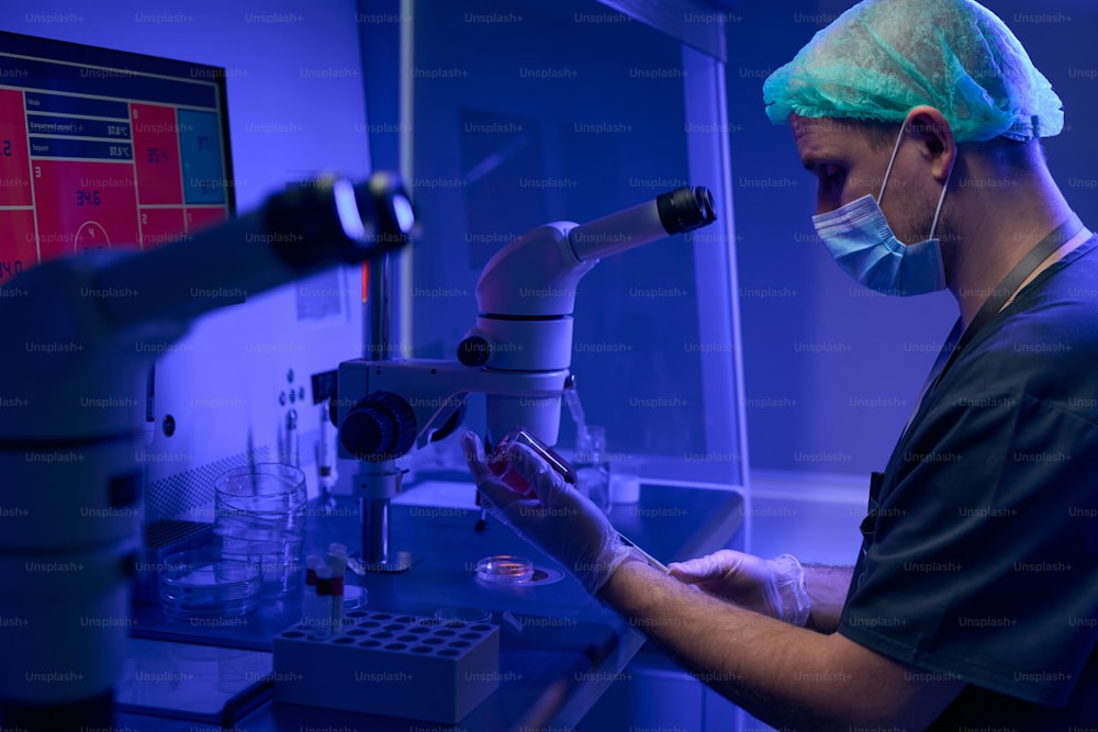 顕微鏡で検査するために臍帯血サンプルを準備する保護フェイスマスクと手袋を着用した科学者実験室の労働者