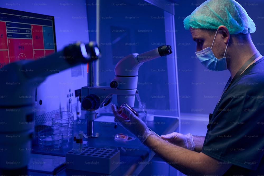 Worker of scientist laboratory in protective face mask and gloves preparing cord blood sample to examine under microscope