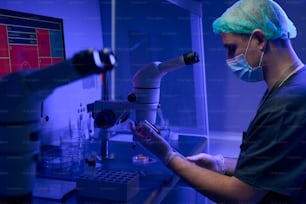 Mitarbeiter des Wissenschaftlerlabors in Schutzmaske und Handschuhen bereitet eine Nabelschnurblutprobe vor, die unter dem Mikroskop untersucht werden soll