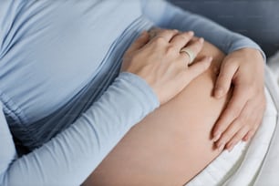 Nahaufnahme einer jungen schwangeren Frau mit Händen auf dem Bauch, pastellblaue Töne