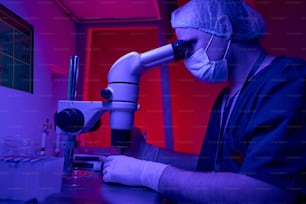 Científico de laboratorio médico que mantiene las investigaciones observando cuidadosamente en el microscopio las células germinales, trabajando con material de ADN
