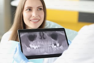 Portrait of dental consultation in clinic and doctor examine teeth x ray on digital tablet screen. Stomatologist on appointment with patient. Teeth concept