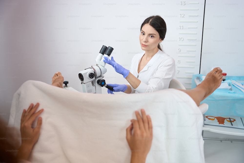 Female gynecologist is siting and making an examination of the patient uterus using a microscope