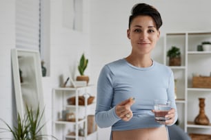 朝に出生前のビタミンとサプリメントを服用している妊娠中の若い女性の腰の肖像画はカメラに微笑んでいます
