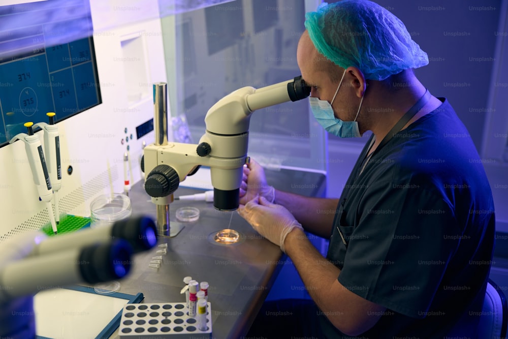 Embryologist researching female cells and preparing them for biopsy and fertilization, working at biolaboratory with microscope and digital monitors