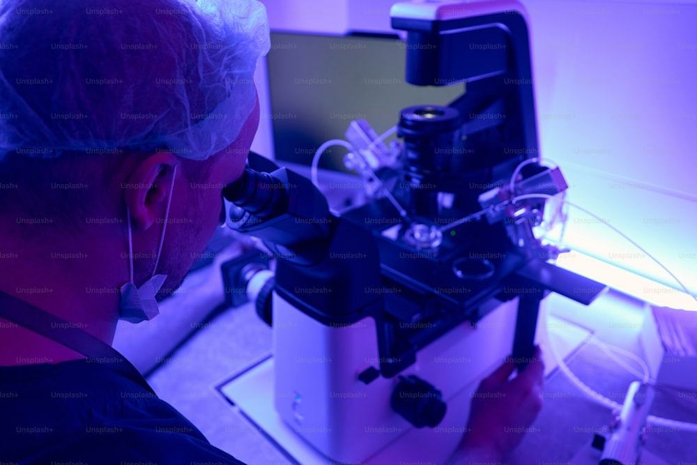 Man laboratory technician adjusting microscope with micromanipulator before working with stem cells or embryos